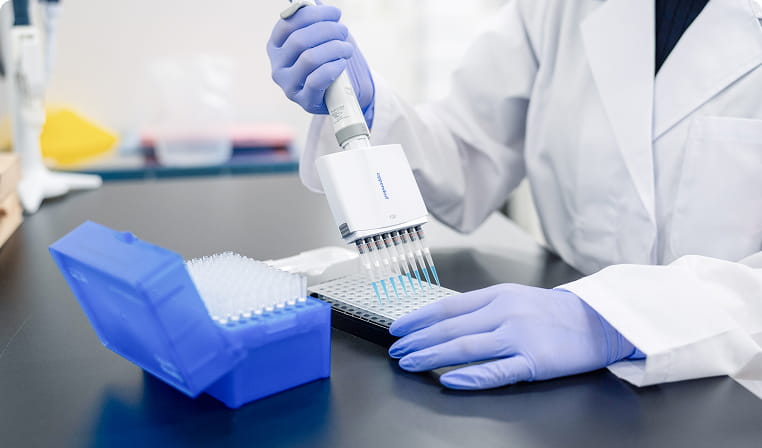 研究者が白衣と青い手袋を着用し、マルチチャンネルピペットでプレートに液体を分注している