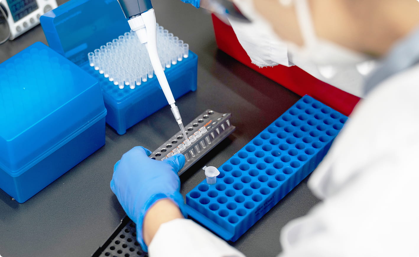 青いグローブを着けた研究者が、ピペットで試薬をチューブに分注している