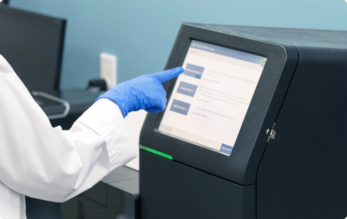 青いグローブを着けた研究者が、タッチパネル式の黒い機器を操作している