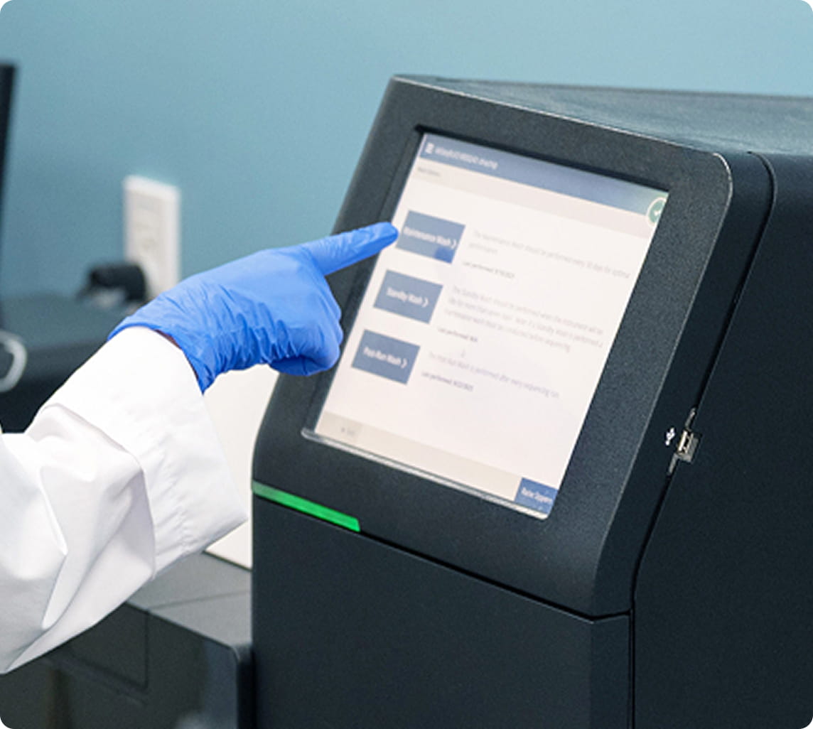 青い手袋をした研究者が、黒い分析機器のタッチパネルを指で操作している